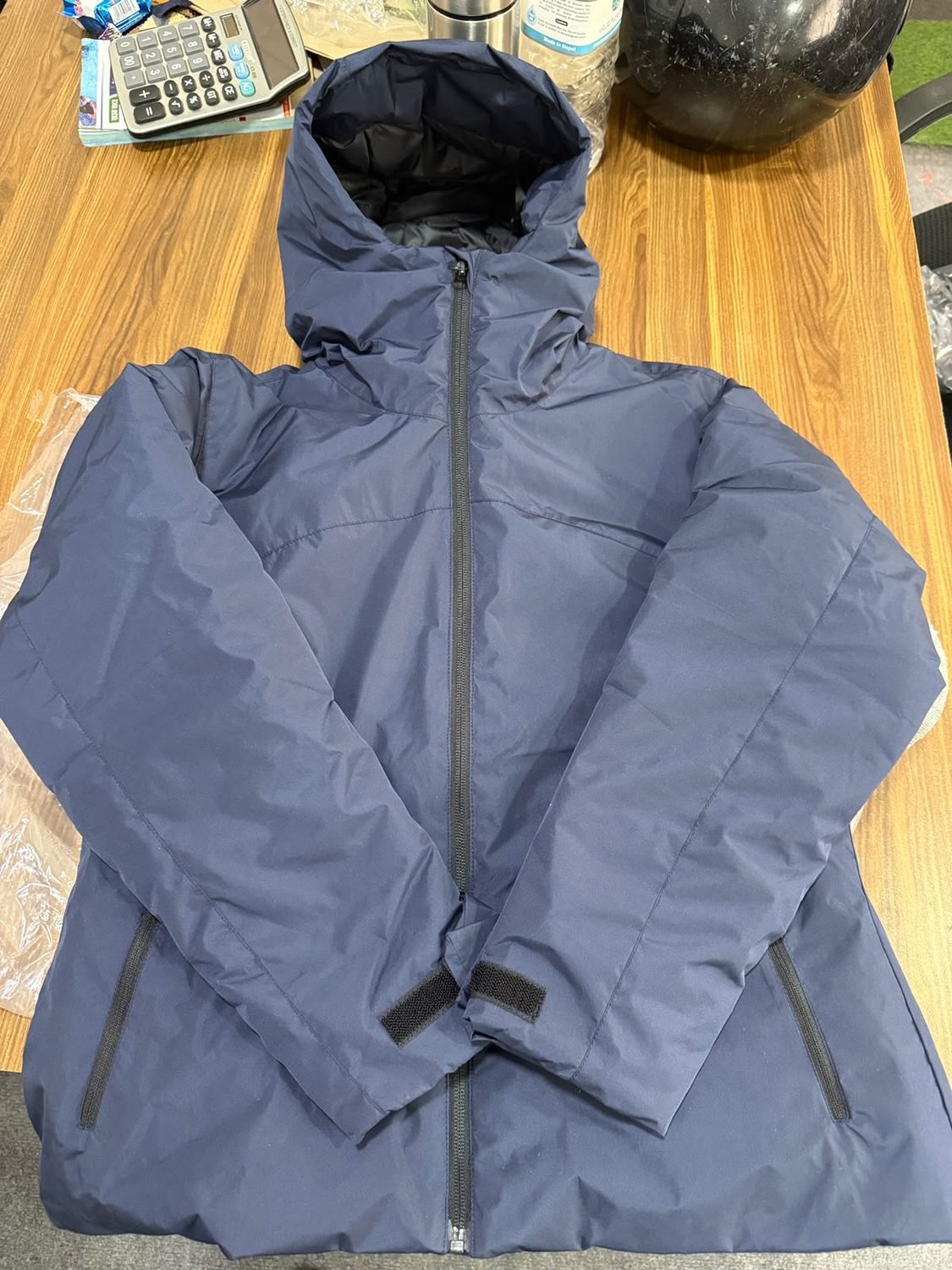 A blue grey down hooded jacket laid flat on a wooden table