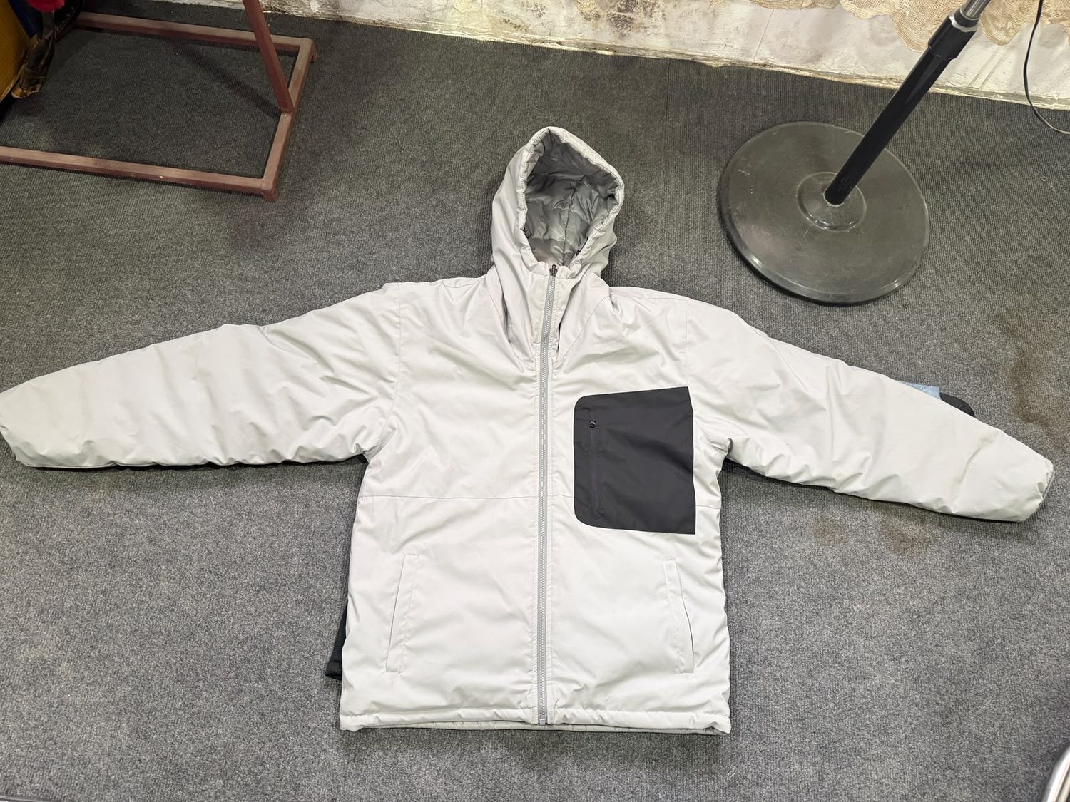 An off white hooded jacket laid flat on grey carpet with a large black chest pocket panel