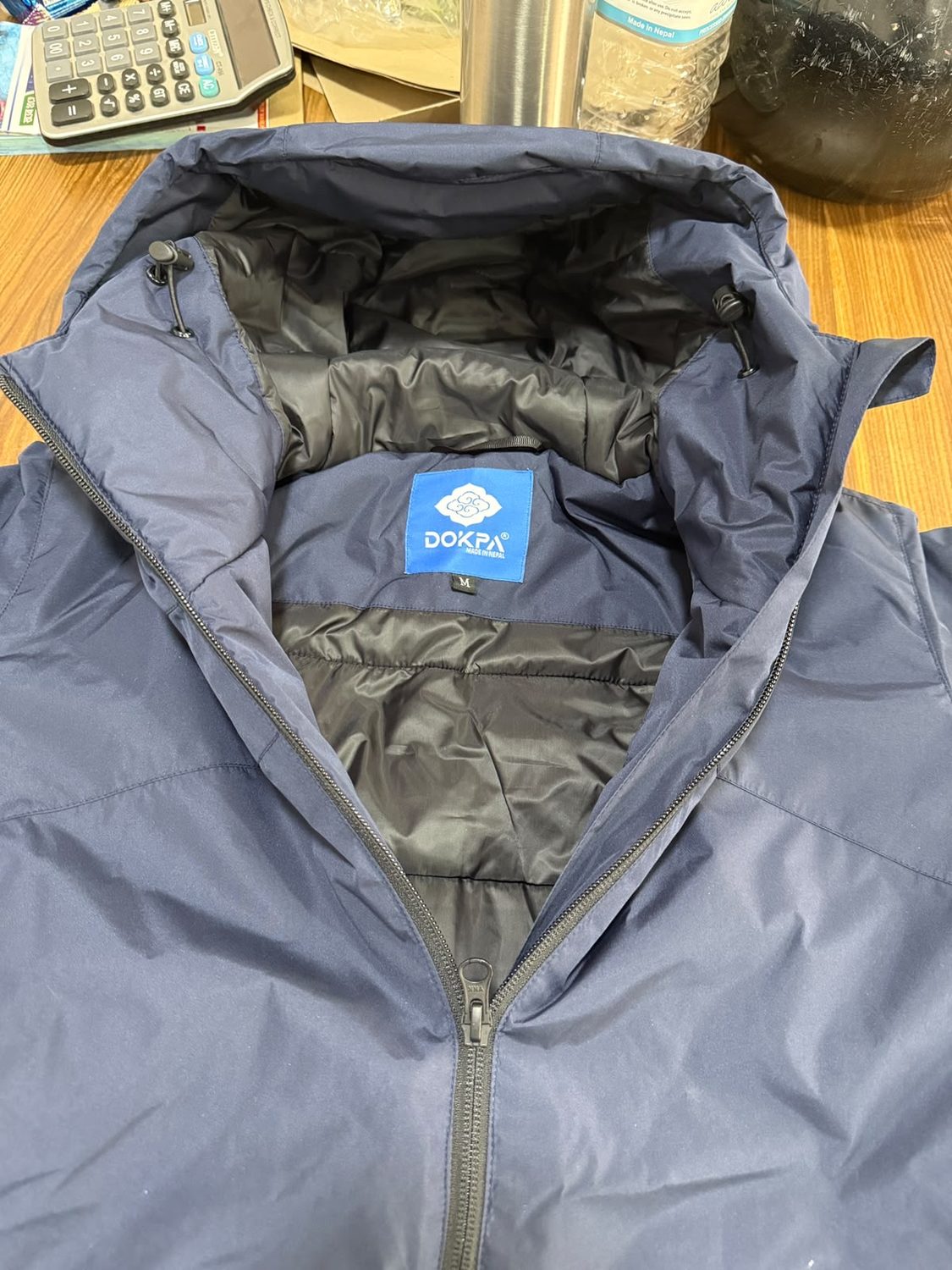 Close view of the blue Dokpa Made in Nepal woven label stitched inside a jacket hood