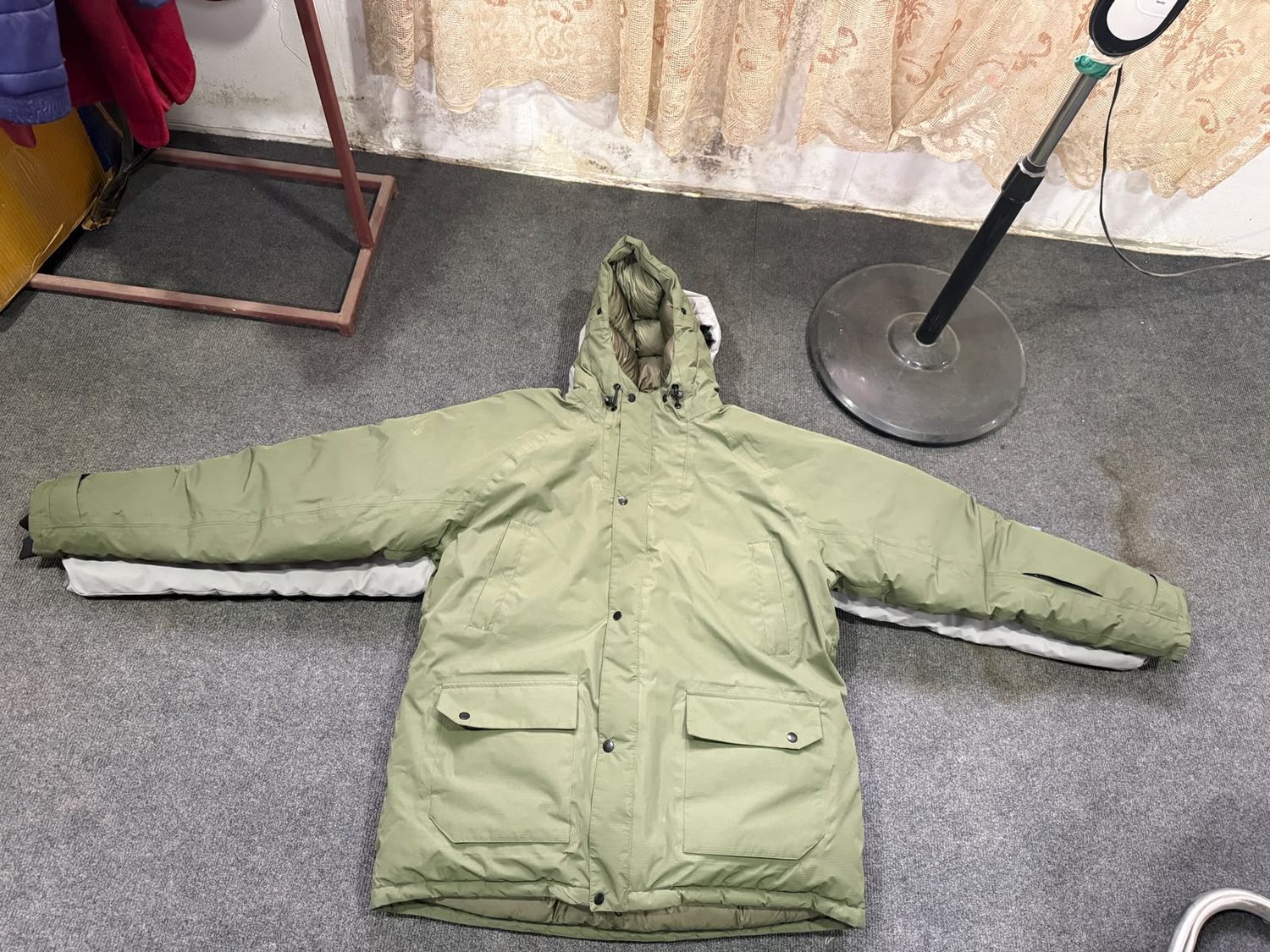 An olive green hooded parka laid flat, showing the front zip and lower pockets