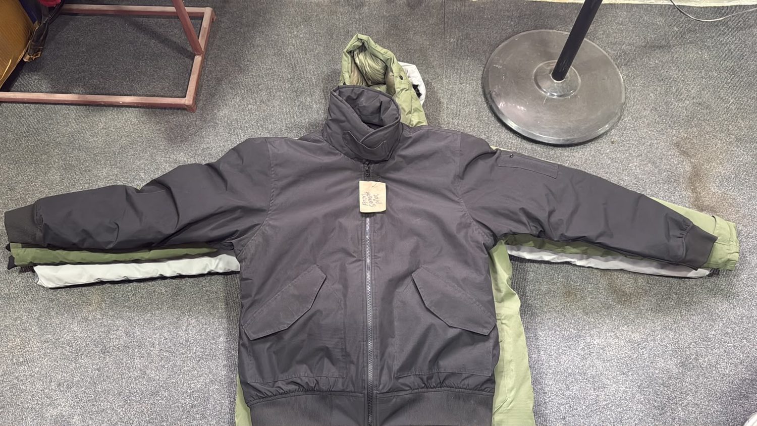 A charcoal hooded shell jacket laid flat, with a second olive lined jacket underneath it