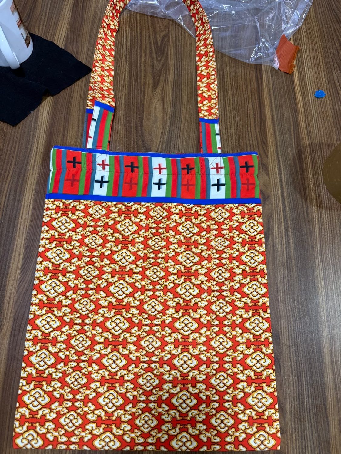 A tote bag made from red and gold patterned cloth with a striped woven band across the top